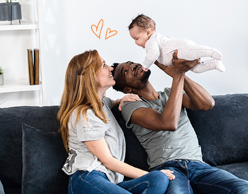 A man and woman happily hold their baby while they are seated on a sofa